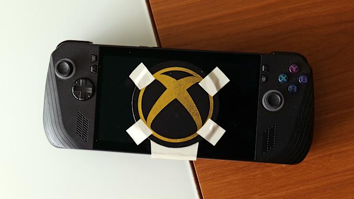 A black and gold Xbox logo duct-taped onto the screen of a gaming handheld device.