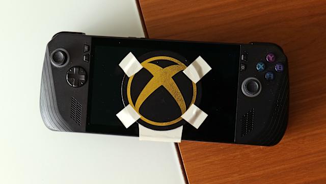 A black and gold Xbox logo duct-taped onto the screen of a gaming handheld device.