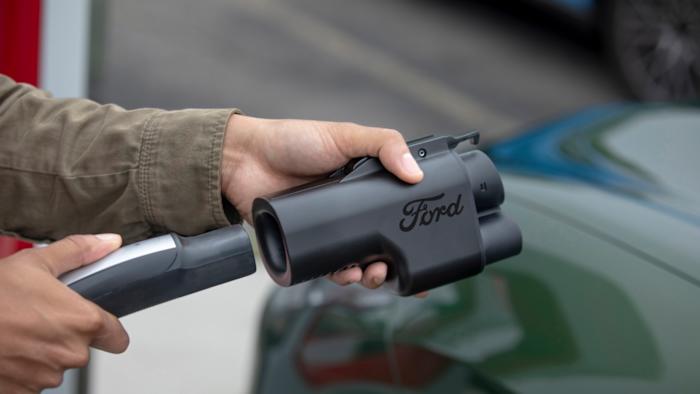Hands holding a charging line and a Ford-branded charging adapter.