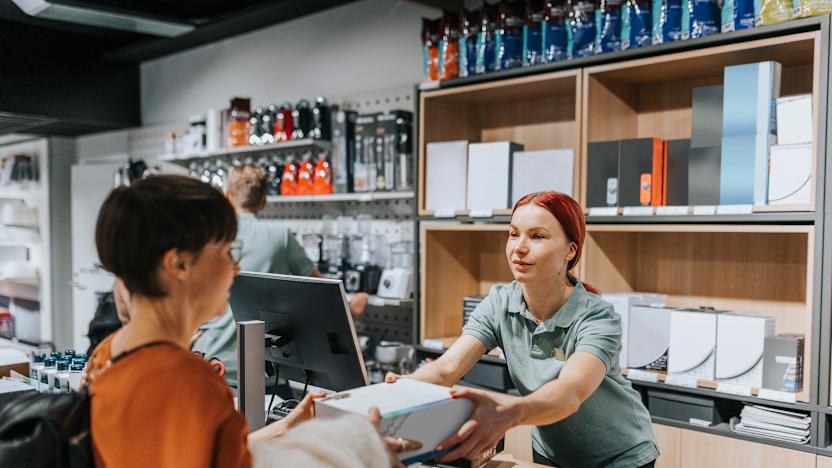 Female customer giving appliance box to sales clerk at checkout counter in electronics store