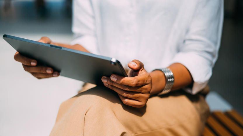 A close up view of an unrecognizable Latin entrepreneur read something on her tablet while sitting on the street bench.