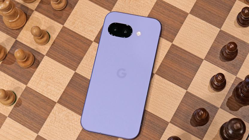 The purple Pixel 9a laying on the middle of a chess board, with black and white chess pieces on either side. The phone's screen is facing down.