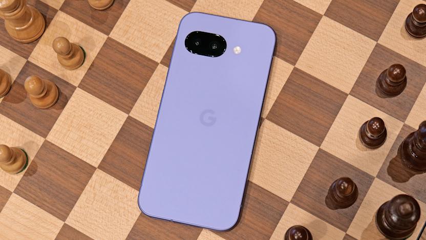 The purple Pixel 9a laying on the middle of a chess board, with black and white chess pieces on either side. The phone's screen is facing down.