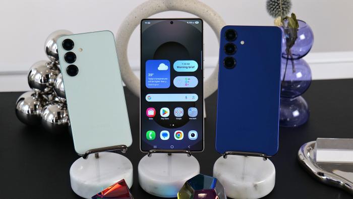 The Samsung Galaxy S25 lineup is displayed on a table with shiny baubles on it. The Galaxy S25, S25+ and S25 Ultra are shown. 