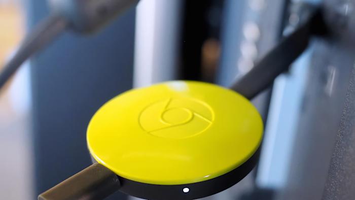 A yellow second-generation Chromecast plugged in to a TV.