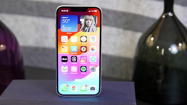 The iPhone 16e standing on a book with its home screen facing front.